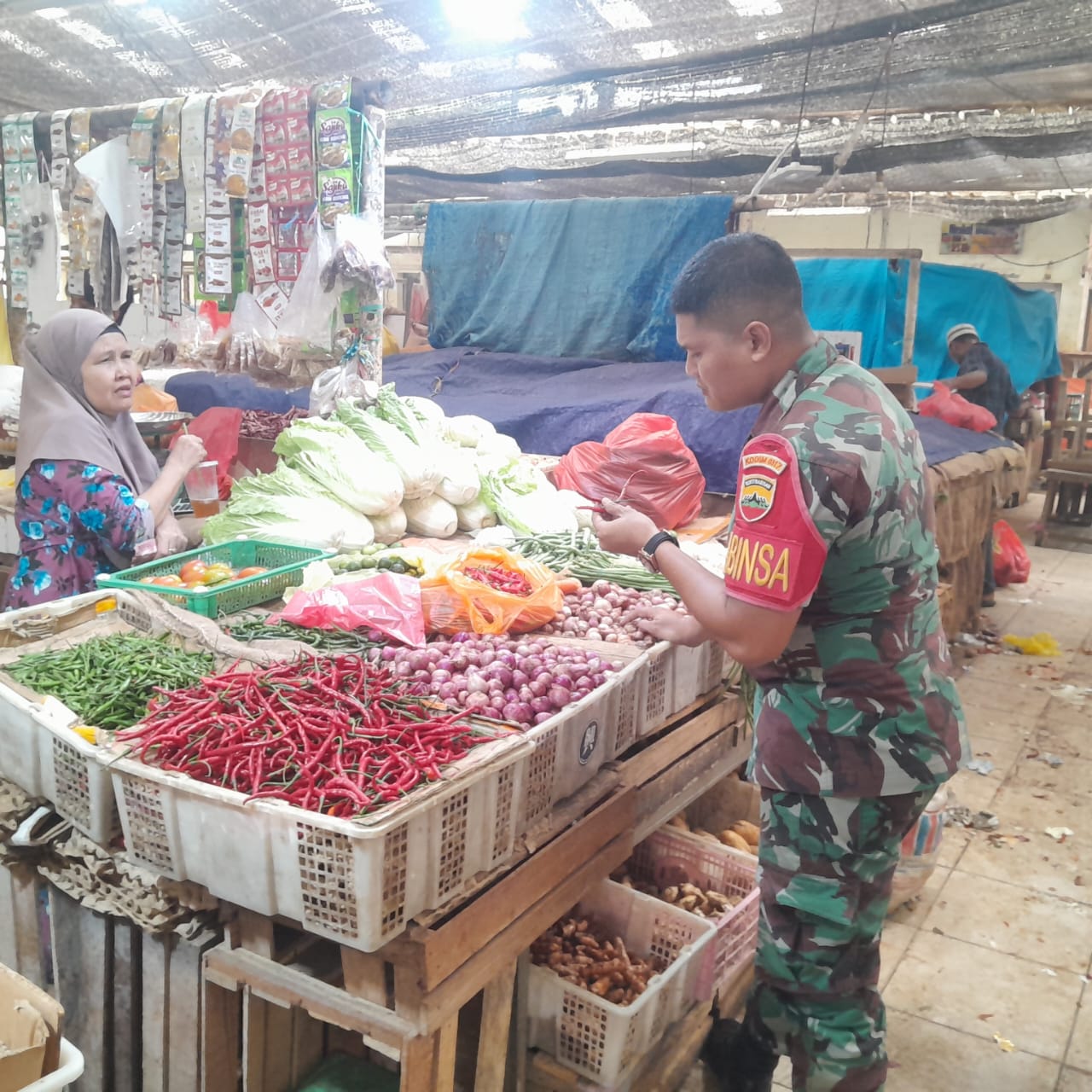 Babinsa Kelurahan Sungai Pasir, Kopda Hasibuan, Komsos dengan salah satu warga, Ibu Siti, seorang pedagang sayuran berusia 46 tahun.
